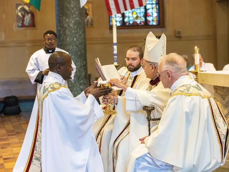 Bishop Mark J. Seitz of El Paso, Texas, presents a chalice and paten to Maryknoll Father Patrick Okok.