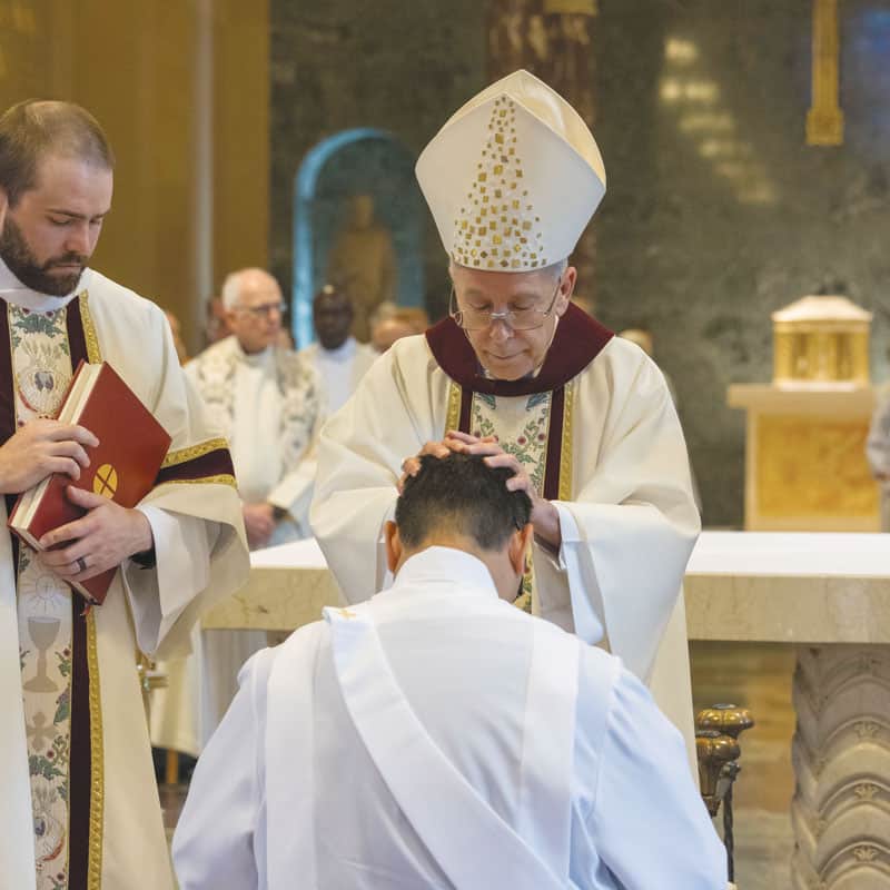 El Obispo Seitz, prelado ordenante, impone las manos sobre Matthew Sim, quien fue ordenado sacerdote con Patrick Okok el 7 de junio. (Octavio Durán, OFM/EE.UU.)