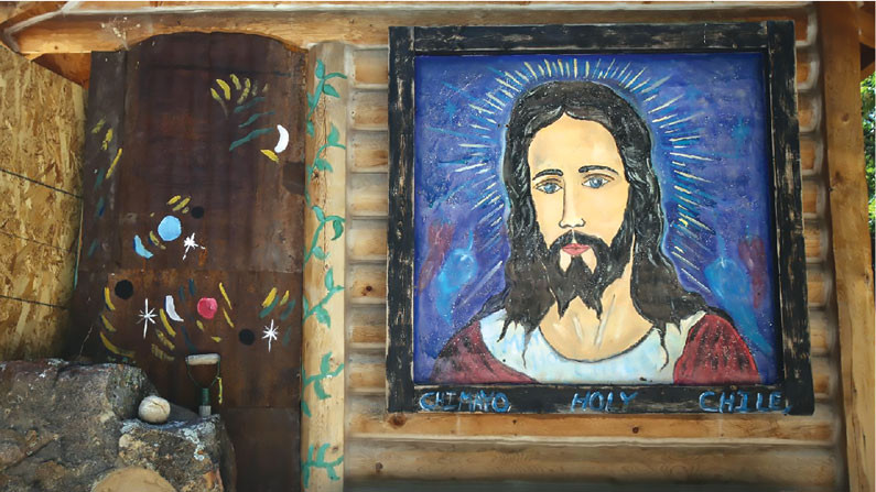 A large, colorful, hand painted picture of Jesus hangs on the side of a wooden building.