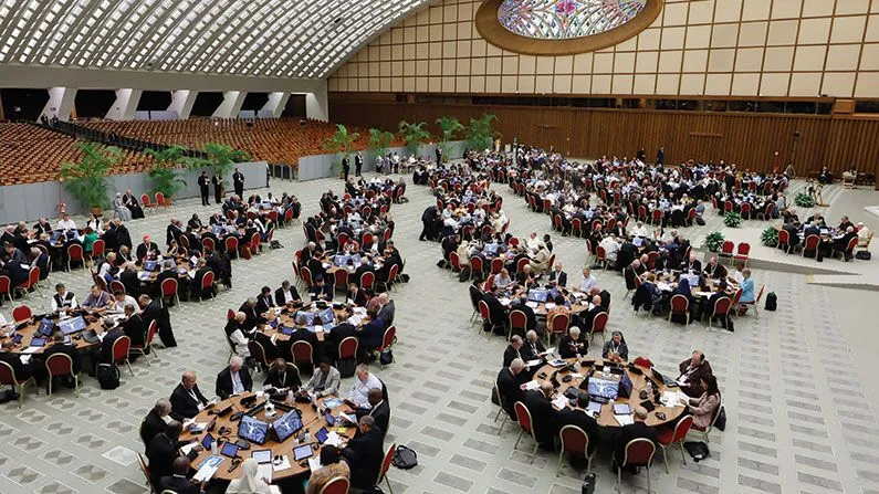 Hundreds of people sitting at dozens of round tables in a huge meeting room.