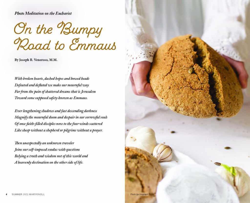 a unseen person in a white shirt with lace cuffs breaks the bread over a white tablecloth next to garlic and another loaf of bread