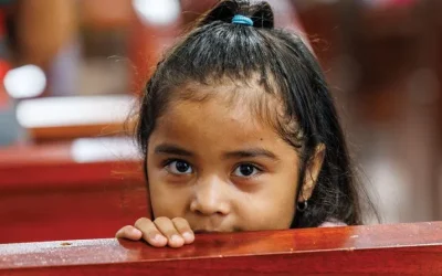 A young girl peeks her head over the top of a church pew