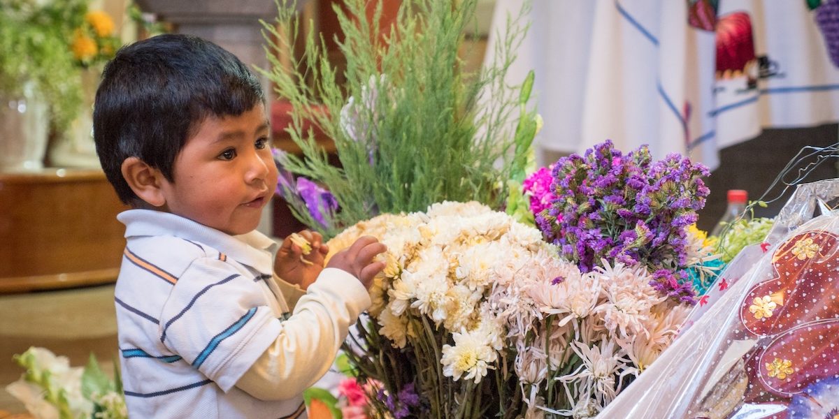 A little boy stands next to flowers during the All Saints Day Mass at a Maryknoll church in Jayllihuaya, Puno Department, Peru. (Nile Sprague/Peru)