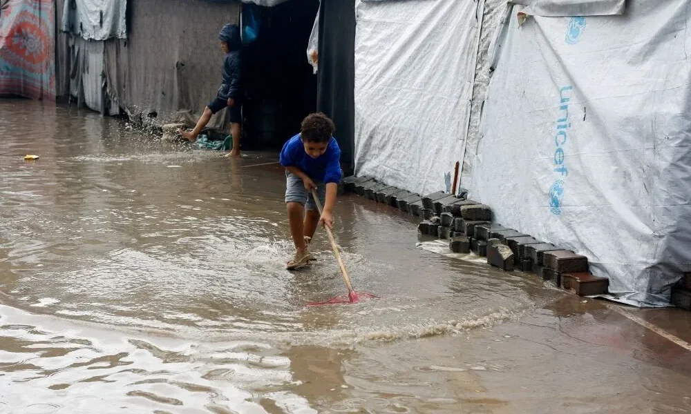 A young boy walks through a flooded path between UNICEF tents in Gaza.