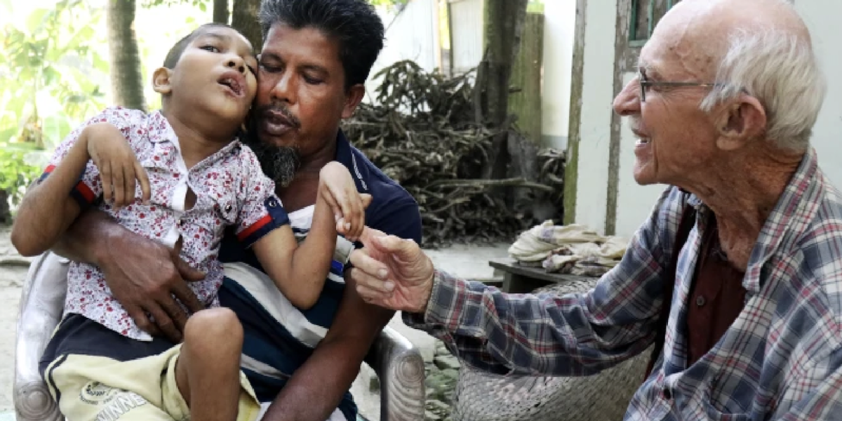 Abdul Mannan Khan and his disabled son Abu Mosa Khan meet with Maryknoll Father Robert McCahill at their home in Munshigonj district, Bangladesh, on Nov. 18, 2025. The priest visits villages daily to find disabled children and connect them with medical treatment. (Stephan Uttom Rozario/Bangladesh)