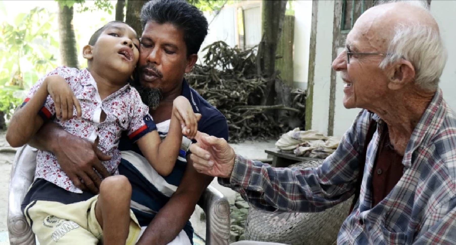 Abdul Mannan Khan and his disabled son Abu Mosa Khan meet with Maryknoll Father Robert McCahill at their home in Munshigonj district, Bangladesh, on Nov. 18, 2025. The priest visits villages daily to find disabled children and connect them with medical treatment. (Stephan Uttom Rozario/Bangladesh)