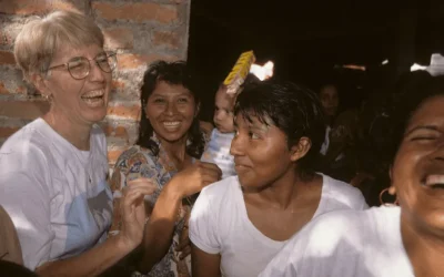 A group of women, one with a baby, smile and laugh as they walk out of church.