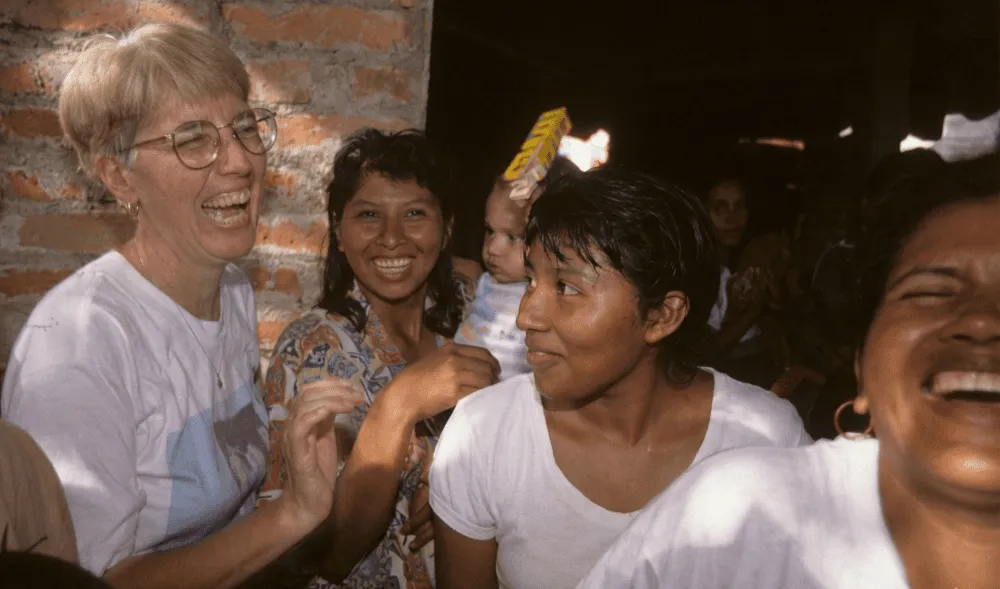 A group of women, one with a baby, smile and laugh as they walk out of church.