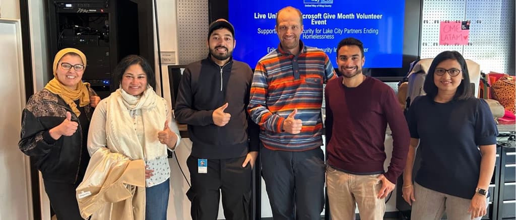 Three young men and a women give a thumbs-up sign towards the camera at a meeting.