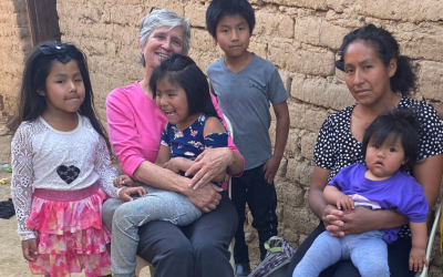Maryknoll Lay Missioner Louise Locke (in pink shirt) visits with Lourdes and her children in a poor community on the outskirts of Cochabamba, Bolivia. Lourdes, who has five young children including one with a developmental disability, was given a small cart for selling street food to support her family. (Courtesy of Louise Locke/Maryknoll Lay Missioners/Bolivia)
