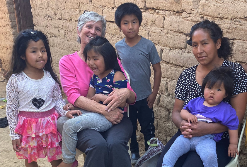 Maryknoll Lay Missioner Louise Locke (in pink shirt) visits with Lourdes and her children in a poor community on the outskirts of Cochabamba, Bolivia. Lourdes, who has five young children including one with a developmental disability, was given a small cart for selling street food to support her family. (Courtesy of Louise Locke/Maryknoll Lay Missioners/Bolivia)