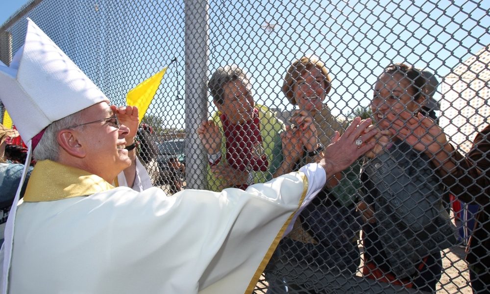 Bishop Mark J. Seitz of El Paso, Texas, is pictured in a file photo touching the hands of people in Mexico through a border fence following Mass in Sunland Park, New Mexico. (OSV News/Bob Roller)