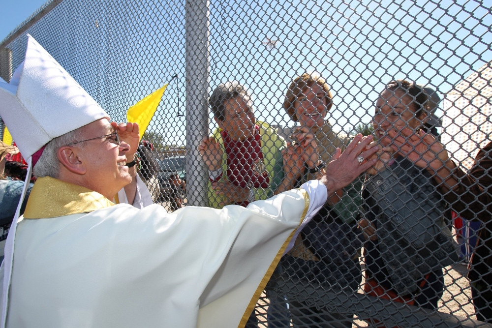 Bishop Mark J. Seitz of El Paso, Texas, is pictured in a file photo touching the hands of people in Mexico through a border fence following Mass in Sunland Park, New Mexico. (OSV News/Bob Roller)