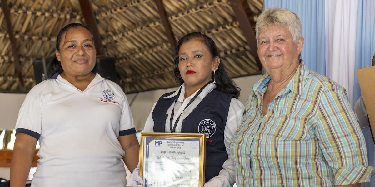 Luz Elizabeth “Lux” Hernández (left) and Maryknoll Sister Delia “Dee” Smith (right) formally instate a candidate as a community legal promoter, conferring a vest, identification badge and diploma. The program led by Lux and Sister Dee culminated in a graduation ceremony for 18 participants on Aug. 15, 2024, in the town of Pajapita in the department of San Marcos, Guatemala. (Octavio Durán/Guatemala)