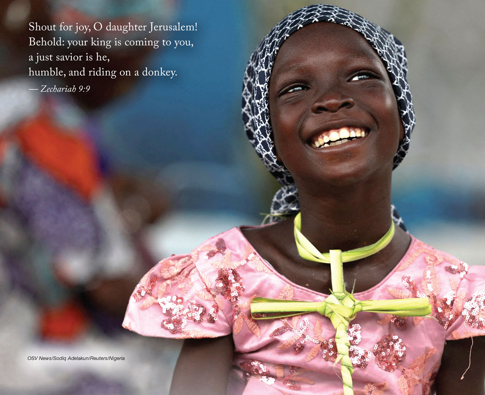 A Nigerian girl smiling, wearing  a cross on a necklace made of palm fronds. 