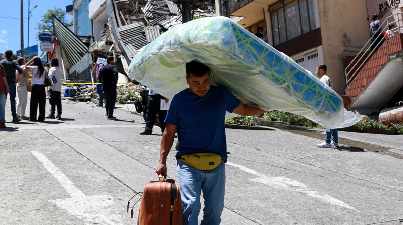 A man carries a mattress down the street in front of damaged buildings after an earthquake, in Manizales, Colombia, Aug. 10, 2026. (OSV News/Andres Camilo Valencia, Reuters)