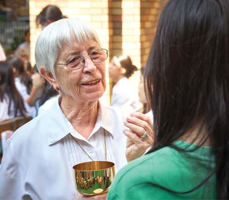 La Hermana Maryknoll Susan Glass, consejera espiritual en Maryknoll Convent School, da la Comunión a una estudiante de secundaria tras la Misa de Todos los Santos en la escuela. (Paul Jeffrey/Hong Kong)