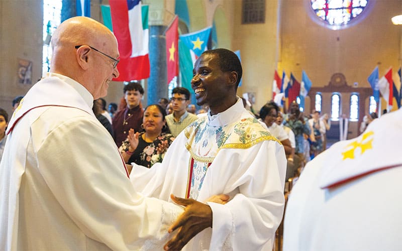 El Padre Charles Ogony saluda al Padre Maryknoll William LaRousse durante el saludo de la paz. (Octavio Durán/Nueva York)