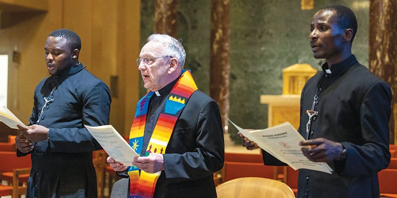 Portando sus crucifijos misioneros, los Padres Maondo y Ogony cantan junto al Superior General Lance Nadeau durante la ceremonia de envío. (Octavio Durán/Nueva York)