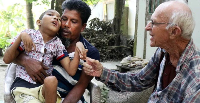 Abdul Mannan Khan y su hijo discapacitado Abu Mosa Khan se reúnen con el Padre Robert T. McCahill en su hogar en el distrito de Munshigonj, Bangladesh, el 18 de noviembre de 2025. El sacerdote visita aldeas a diario para encontrar niños discapacitados y conectarlos con tratamiento médico. (Stephan Uttom Rozario/Bangladesh)