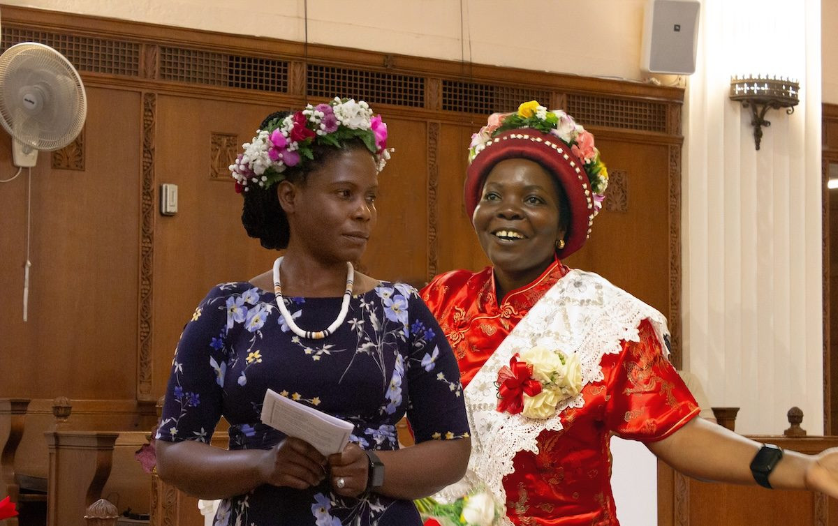 Dos mujeres con conjuntos coloridos y sombreros están de pie en una iglesia.