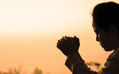 Silueta de una mujer orando a Dios con un atardecer de fondo.