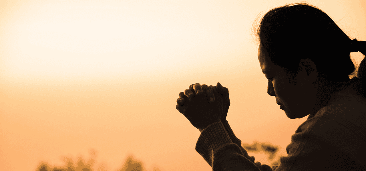 Silueta de una mujer orando a Dios con un atardecer de fondo.