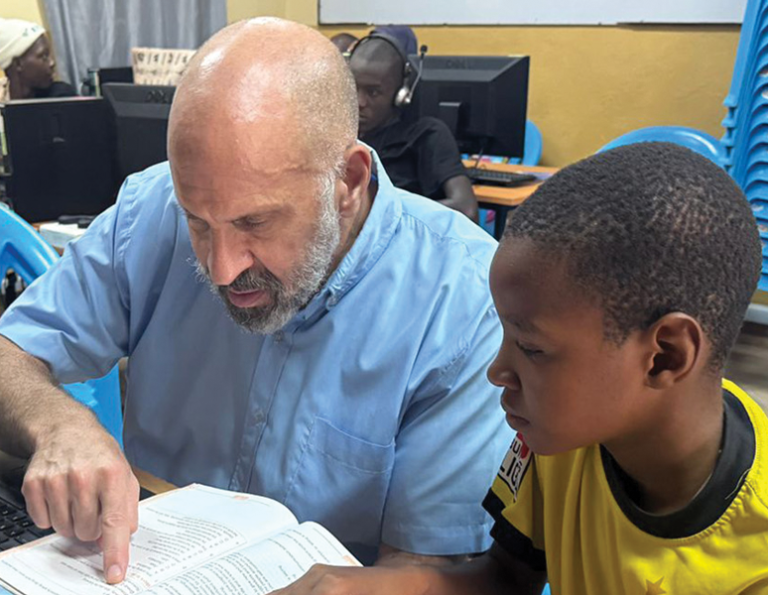 El misionero laico Maryknoll Richard Tarro ayuda a un niño con sus tareas en su misión en Kenia. (Cortesía de Richard Tarro/Kenia)