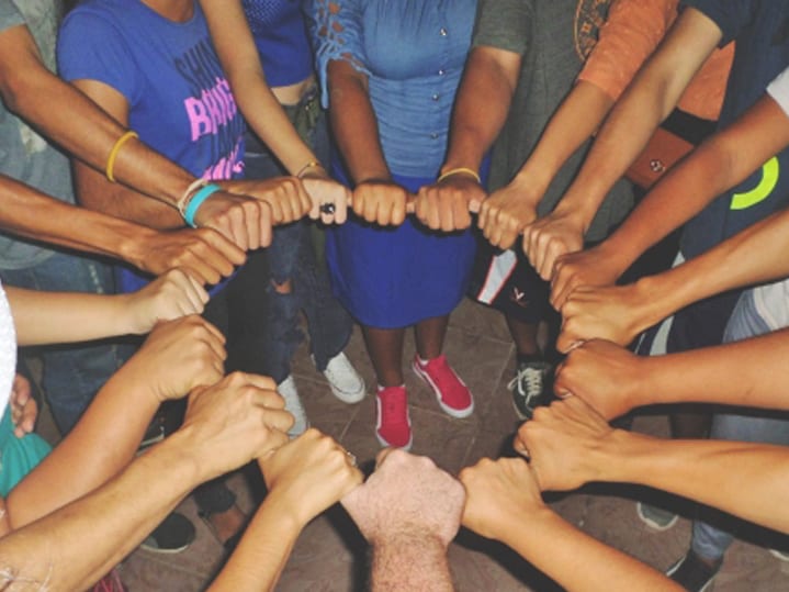 Dos docenas de manos sostienen un objeto cicular y forman un gran anillo que simboliza el trabajo en equipo y la unión.