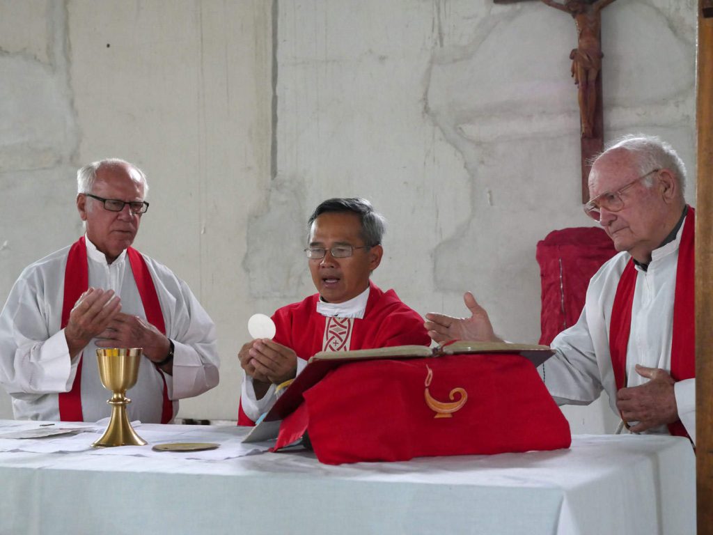 Tres sacerdotes Maryknoll están detrás del altar celebrando misa