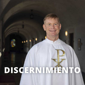 Un sacerdote con túnica blanca de pie en un largo pasillo