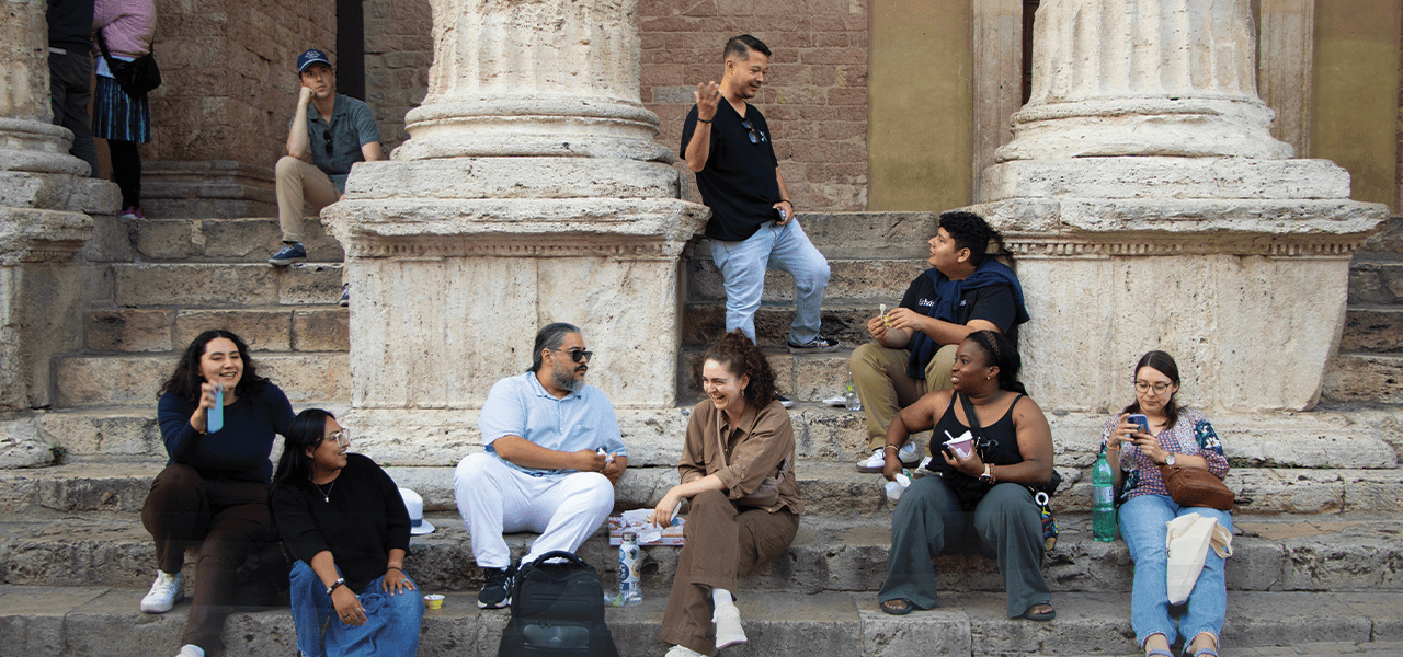Peregrinos de los Jóvenes Adultos Embajadores Maryknoll y Jóvenes Adultos del Catholic Climate Covenant conversan frente a una iglesia en Asís. (Andrea Moreno-Díaz/Italia)