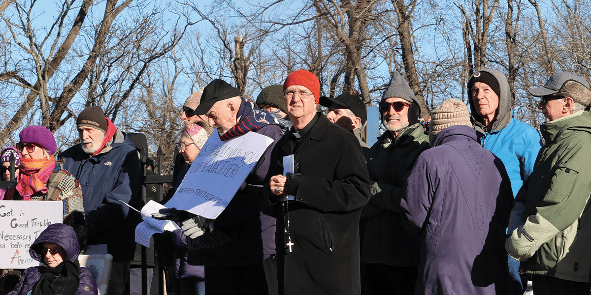 El obispo Bruce Lewandowski (de gorro naranja) de Providence, Rhode Island, dirige una vigilia de oración y rezo del rosario frente a un centro de detención. (Erik Scalavino/EE. UU.)
