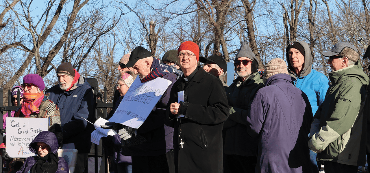 El obispo Bruce Lewandowski (de gorro naranja) de Providence, Rhode Island, dirige una vigilia de oración y rezo del rosario frente a un centro de detención. (Erik Scalavino/EE. UU.)