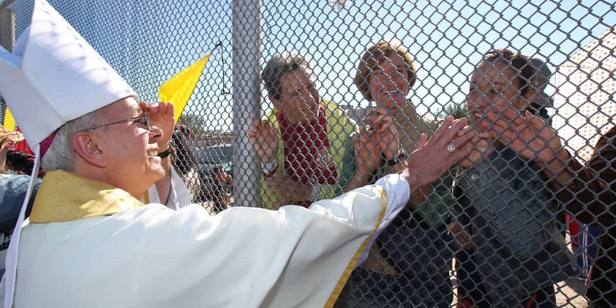 El Obispo Mark J. Setiz de El Paso, Texas, toca las manos de personas en México a través de una reja en la frontera entre Estados Unidos y México después de una Misa en Sunland Park, Nuevo México. (OSV News/Bob Roller)