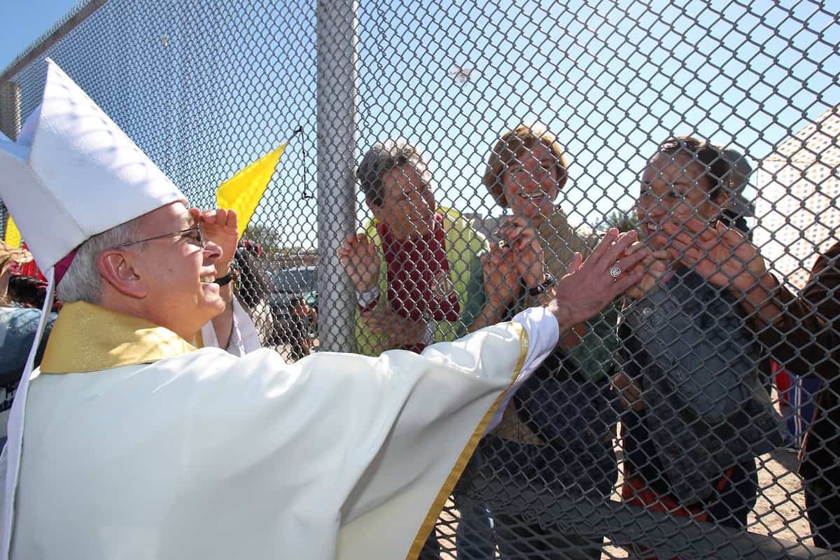 El Obispo Mark J. Setiz de El Paso, Texas, toca las manos de personas en México a través de una reja en la frontera entre Estados Unidos y México después de una Misa en Sunland Park, Nuevo México. (OSV News/Bob Roller)