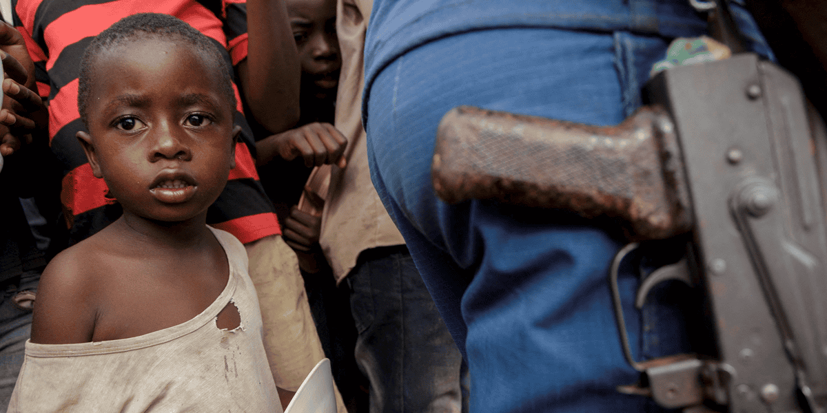 Un niño se encuentra junto a un oficial de la policía mientras familias desplazadas esperan comida en el estadio Rugombo en Burundi el 18 de febrero del 2025, después de que los congoleños huyeran de los nuevos enfrentamientos entre los rebeldes del M23 y las fuerzas armadas de la República Democrática del Congo (FARDC). (OSV News/Evrard Ngendakumana, Reuters)