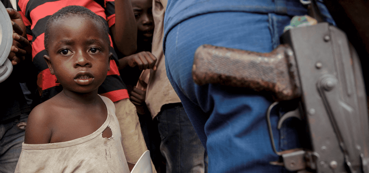 Un niño se encuentra junto a un oficial de la policía mientras familias desplazadas esperan comida en el estadio Rugombo en Burundi el 18 de febrero del 2025, después de que los congoleños huyeran de los nuevos enfrentamientos entre los rebeldes del M23 y las fuerzas armadas de la República Democrática del Congo (FARDC). (OSV News/Evrard Ngendakumana, Reuters)