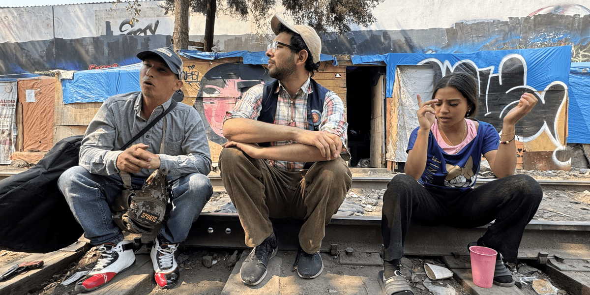 Jesús Ricardo Rojas Romero, de Venezuela, sentado con Mario Monroy, en el centro, e Yesenia, también de Venezuela, en un campamento de migrantes en la Ciudad de México, el 1 de abril de 2025. Monroy, coordinador de divulgación de CAFEMIN, un refugio para mujeres y familias, escucha las necesidades y los sueños ahora destrozados de los migrantes que querían ir al norte, a Estados Unidos, y ahora no pueden ir al sur, de regreso a su país de origen, debido a las restricciones de México al movimiento de los migrantes y a su capacidad para trabajar. (OSV News/Rhina Guidos, Global Sisters Report)