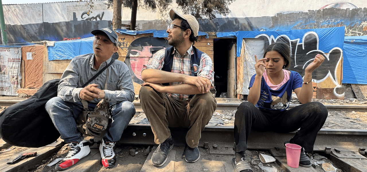 Jesús Ricardo Rojas Romero, de Venezuela, sentado con Mario Monroy, en el centro, e Yesenia, también de Venezuela, en un campamento de migrantes en la Ciudad de México, el 1 de abril de 2025. Monroy, coordinador de divulgación de CAFEMIN, un refugio para mujeres y familias, escucha las necesidades y los sueños ahora destrozados de los migrantes que querían ir al norte, a Estados Unidos, y ahora no pueden ir al sur, de regreso a su país de origen, debido a las restricciones de México al movimiento de los migrantes y a su capacidad para trabajar. (OSV News/Rhina Guidos, Global Sisters Report)