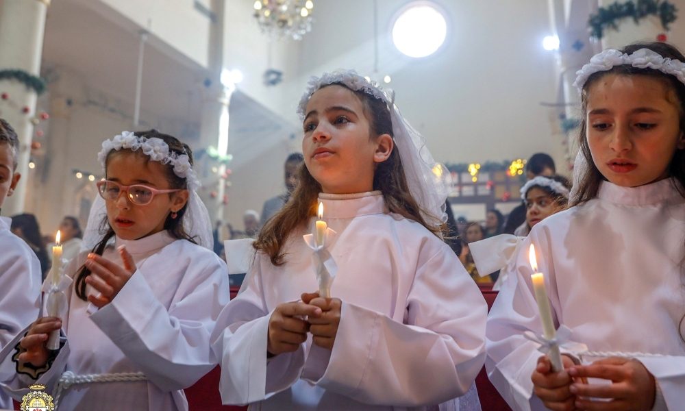 Unas niñas sostienen velas mientras el cardenal Pierbattista Pizzaballa, patriarca latino de Jerusalén, concelebra la misa en la iglesia de la Sagrada Familia, en la ciudad de Gaza, el 21 de diciembre de 2025, durante su visita pastoral navideña. El cardenal visitó antes de Navidad como muestra de cercanía hacia una comunidad que ha soportado dos años de guerra. (OSV News/cortesía del Patriarcado Latino de Jerusalén)