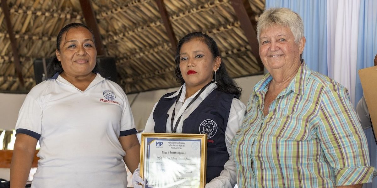 Luz Elizabeth «Lux» Hernández (izq.) y la Hermana Maryknoll Delia «Dee» Smith (dcha.) formalmente incorporan a una candidata como promotora legal comunitaria, otorgándole un chaleco, identificación y diploma. El programa liderado por Lux y la Hermana Maryknoll Dee culminó en una ceremonia de graduación para 18 participantes el 15 de agosto del 2024, en el pueblo de Pajapita en el departamento de San Marcos, Guatemala. (Octavio Durán/Guatemala).