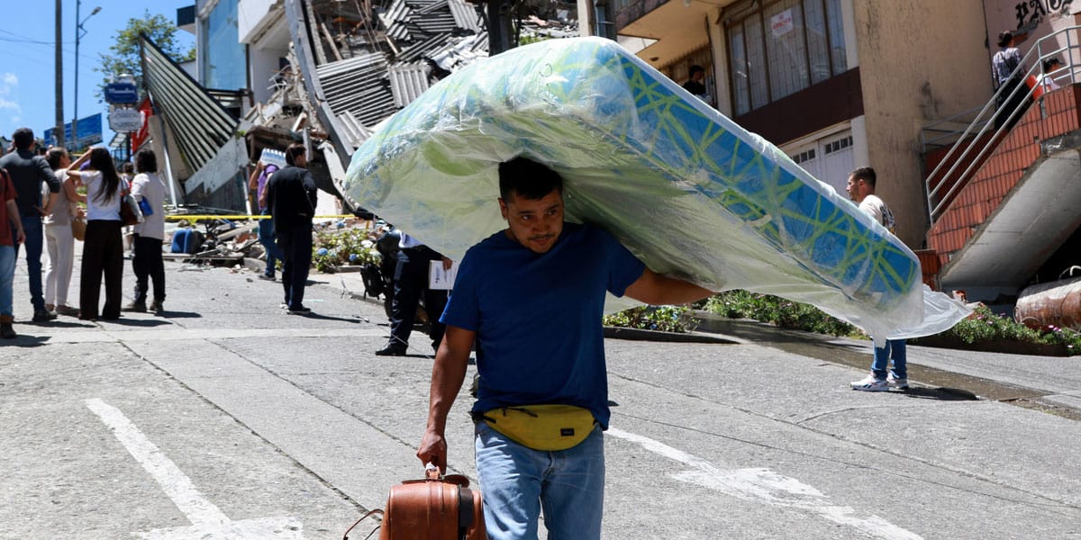 Un hombre carga un colchón por la calle frente a unos edificios dañados tras un terremoto en Manizales (Colombia) el 10 de agosto de 2026. (OSV News/Andrés Camilo Valencia, Reuters)