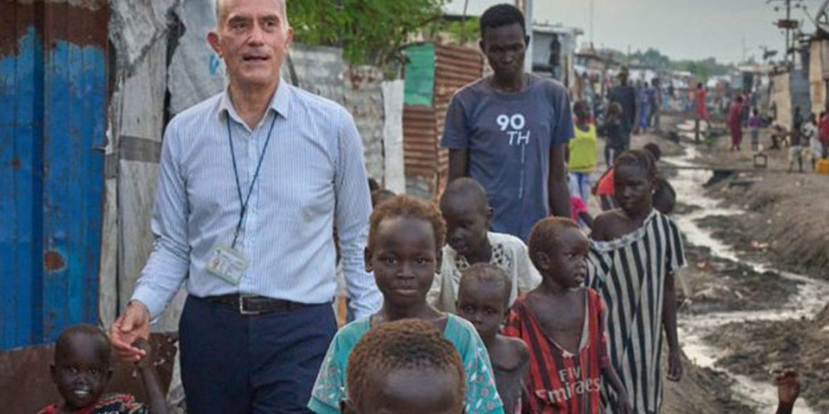 Maryknoll Priest, Fr. Michael Bassano walks with children on a dirt road through makeshift shelters