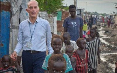 Maryknoll Priest, Fr. Michael Bassano walks with children on a dirt road through makeshift shelters