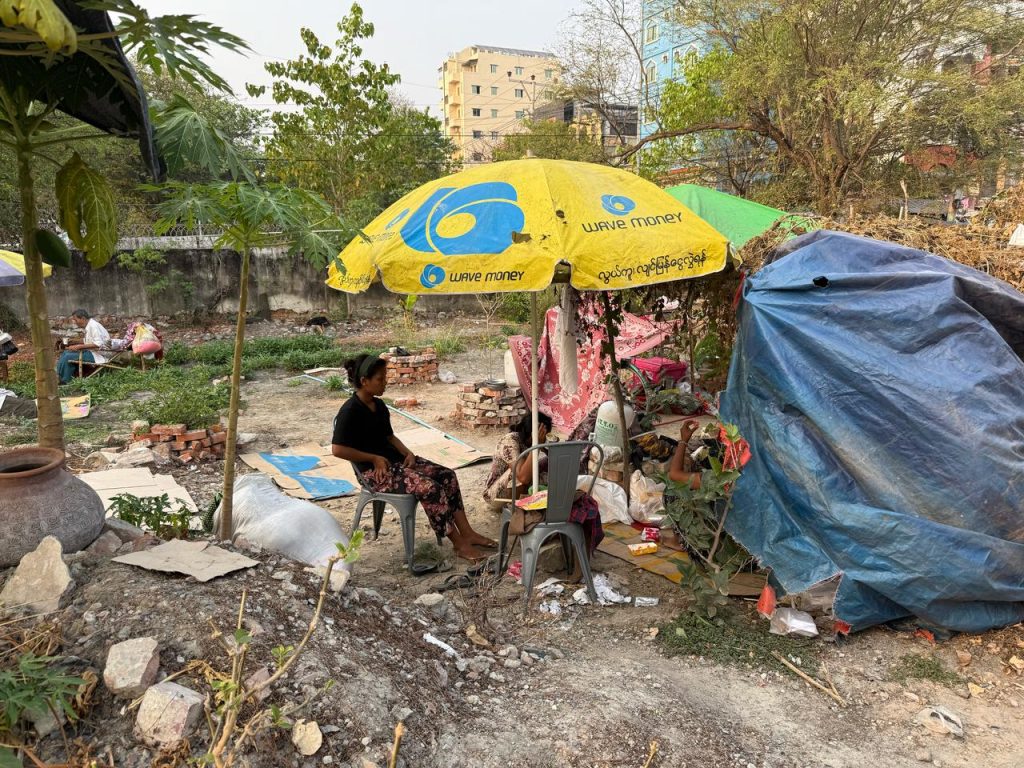 A family seeks shelter in a makeshift shelter made of a tarp and an umbrella.