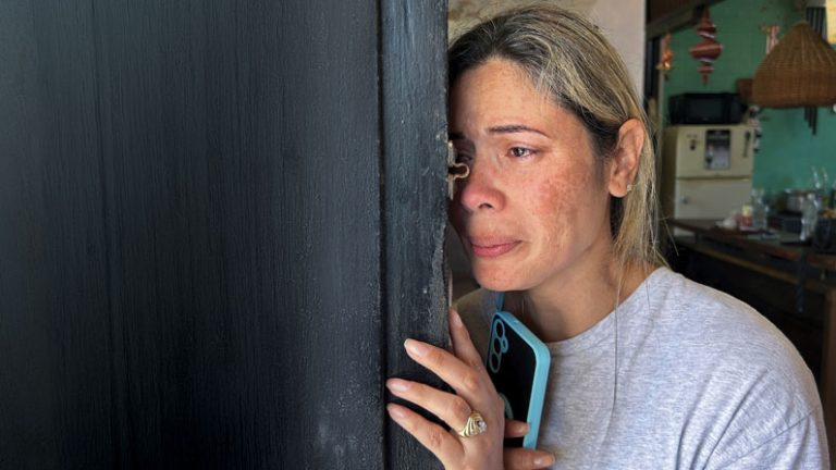 A woman is leaning against an open door crying.