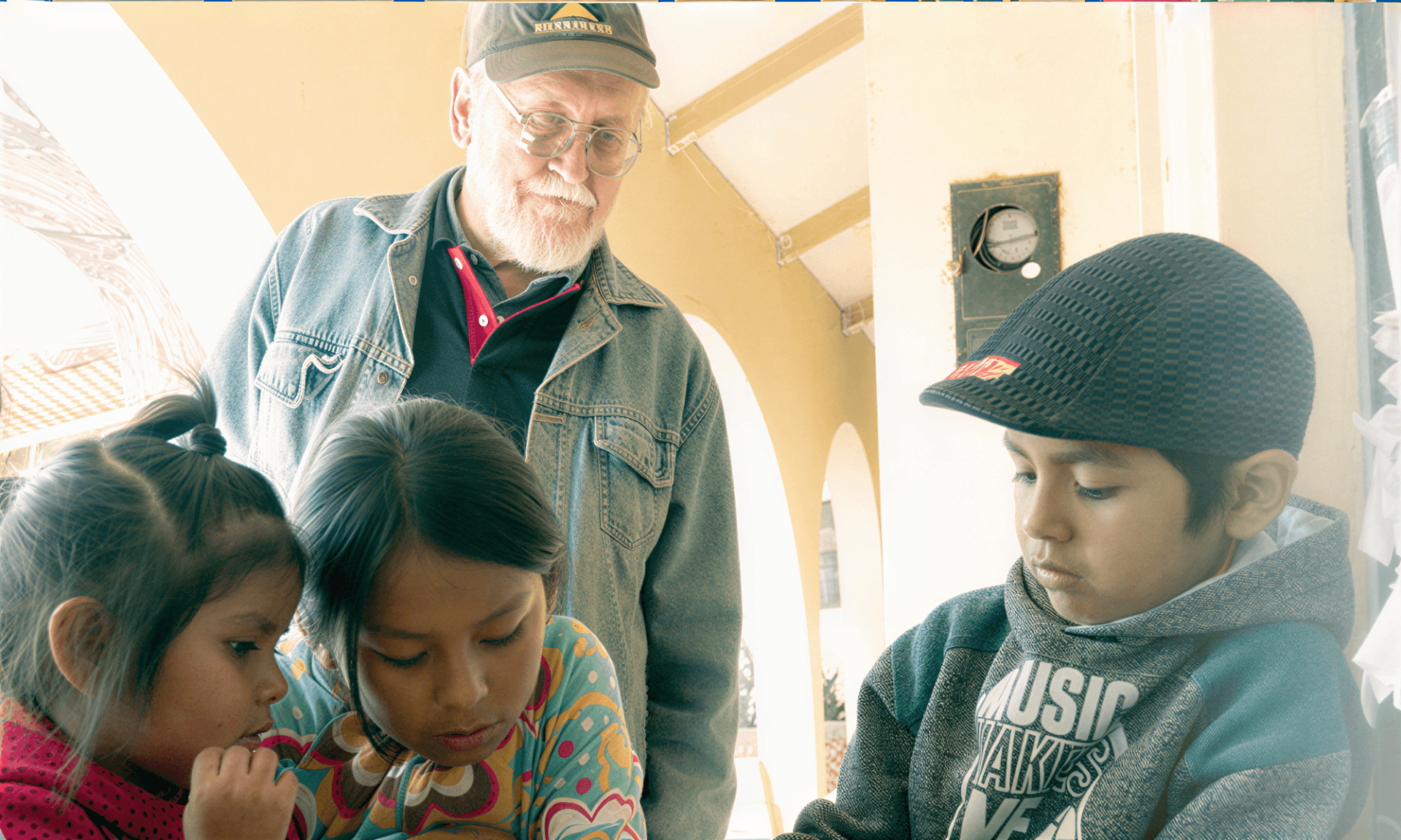 Fr. Paul M. Sykora tutors 3 small children sitting at a table in Bolivia