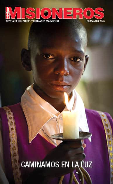The cover of the Maryknoll Magazine Spring 2026 issue with a child dressed in formal white and purple clothes holds a candle and looks directly at the camera.